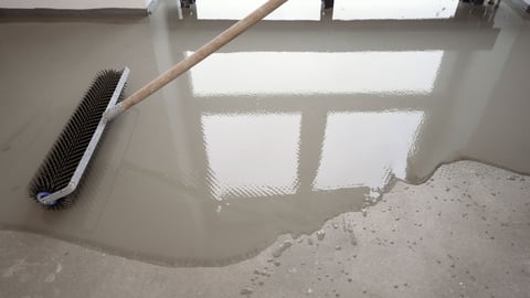 Worker using a spiked roller to level and smooth a concrete surface, ensuring a flat and even finish