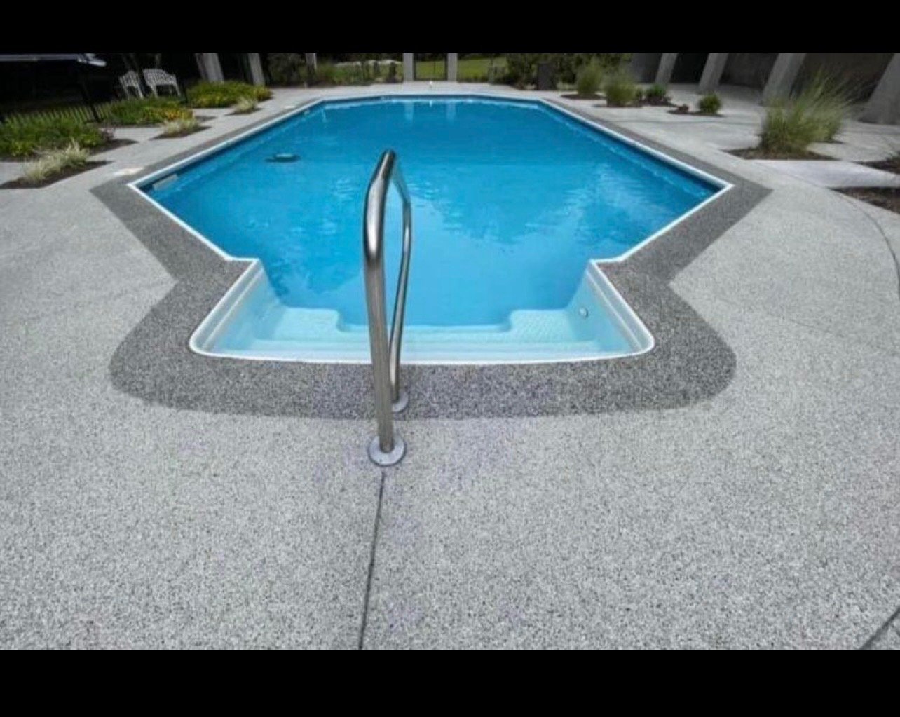 Overhead view of an empty star-shaped swimming pool with a metal slide, surrounded by concrete decking and landscaping