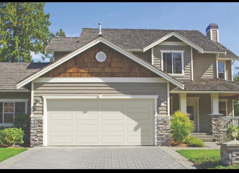 Two-story suburban home with beige siding, stone accents, white garage door, pitched roof, and manicured landscaping