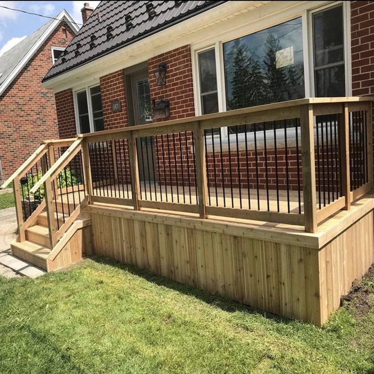 Wooden deck with black railings attached to brick house with large windows and green lawn