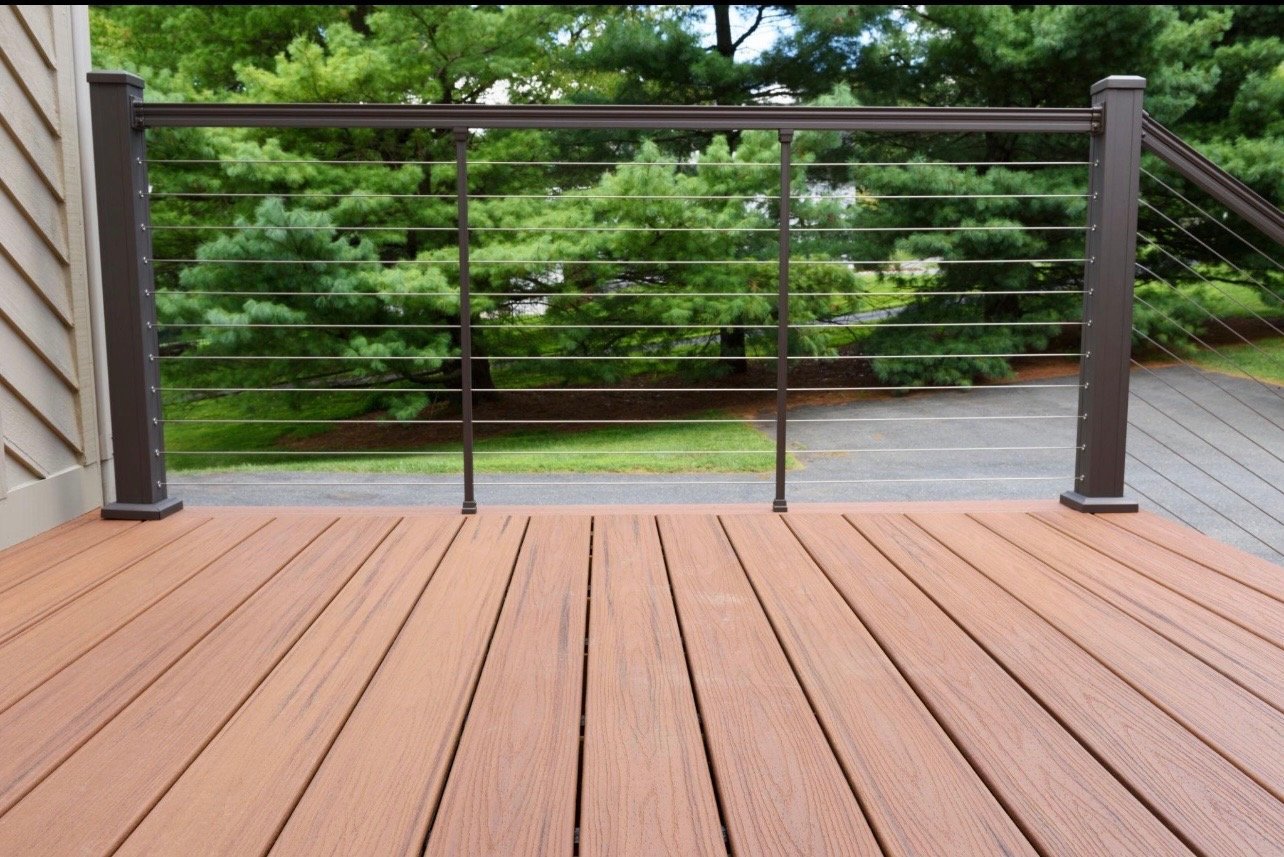 Modern deck with composite wood flooring and black metal cable railing overlooking green landscape and trees