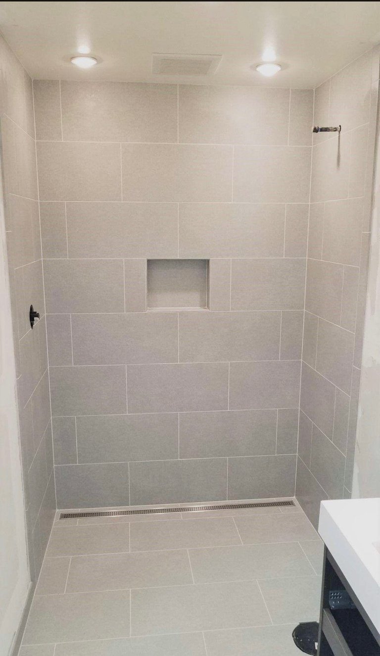 Modern walk-in shower with large format beige tiles, glass enclosure, built-in niche, and recessed lighting