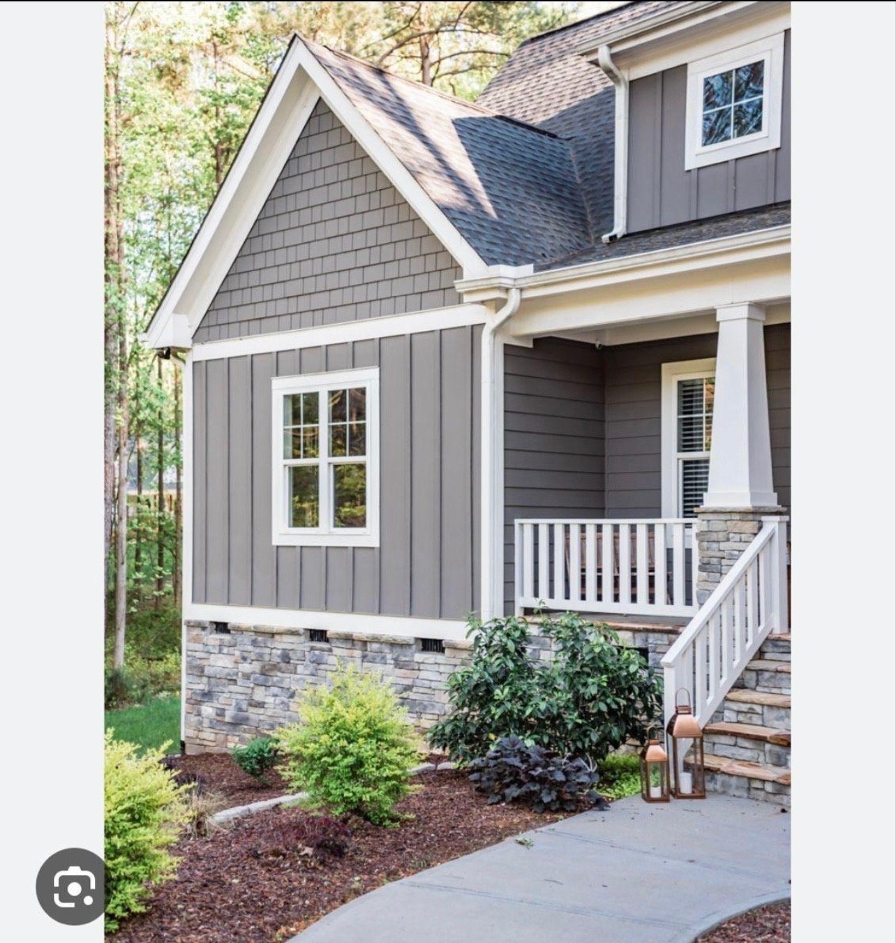 Modern farmhouse exterior with gray and white siding, pitched roof, front porch, white railings, and landscaped front yard with shrubs and mulch