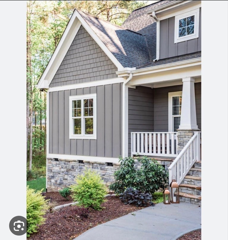 Modern farmhouse exterior with gray and white siding, pitched roof, front porch, white railings, and landscaped front yard with shrubs and mulch