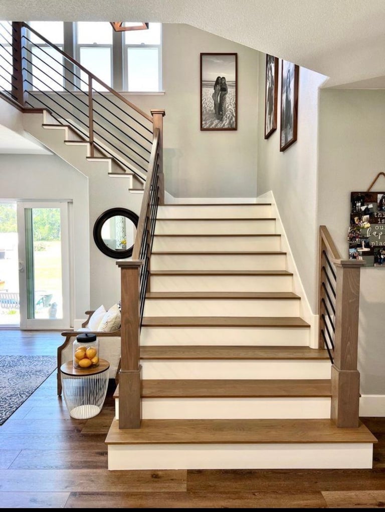 Modern home interior with wooden staircase, metal railing, cream walls, framed artwork, and open floor plan with natural lighting