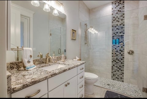 Modern bathroom with white vanity, granite countertop, large mirror with lighting, and walk-in shower