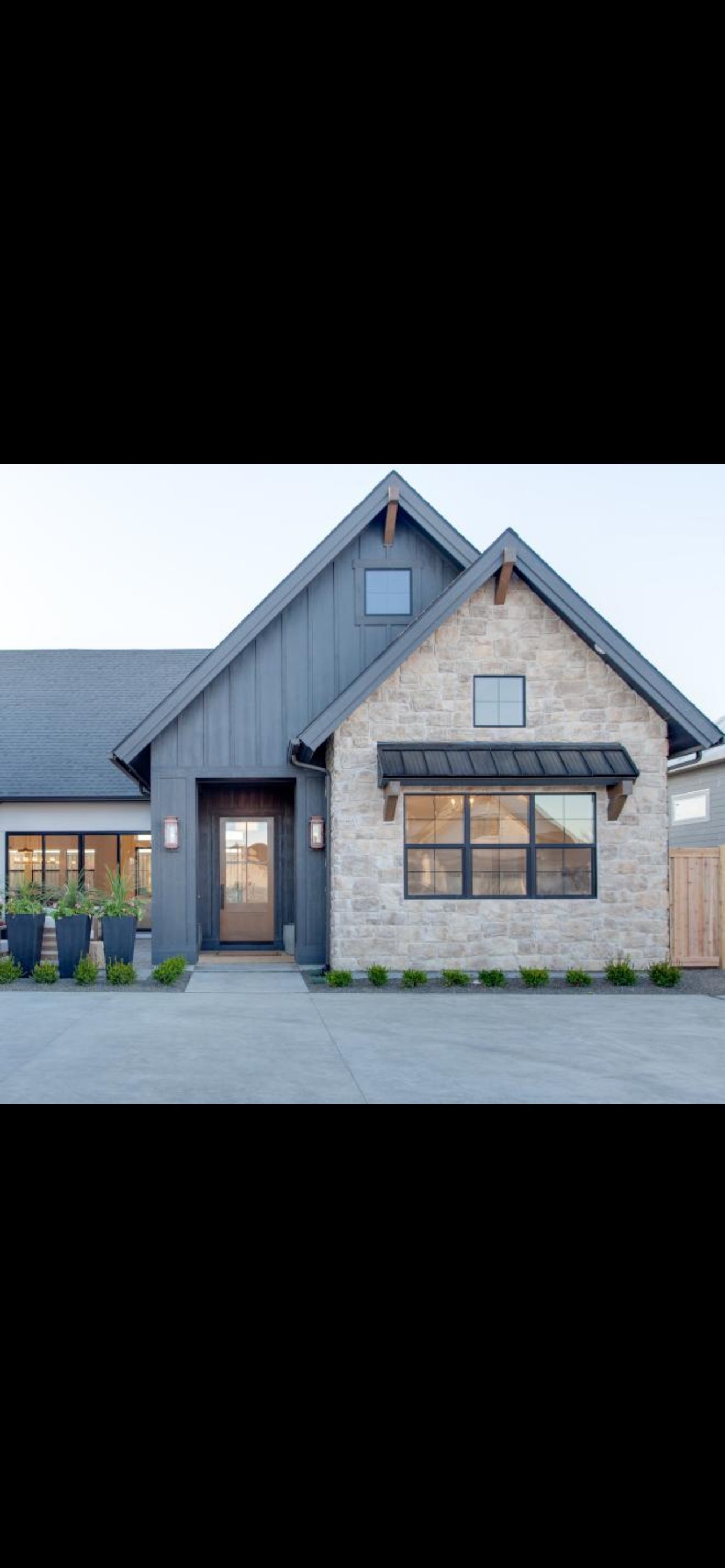 Modern farmhouse exterior with stone and dark blue siding, large windows, peaked roofs, and concrete driveway with landscaping