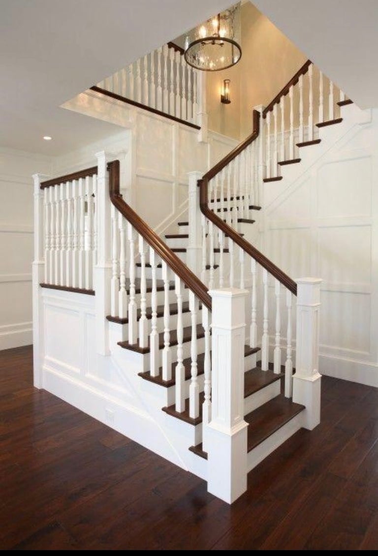 Modern staircase with dark wood railings and white balusters in a bright entryway with pendant light fixture.