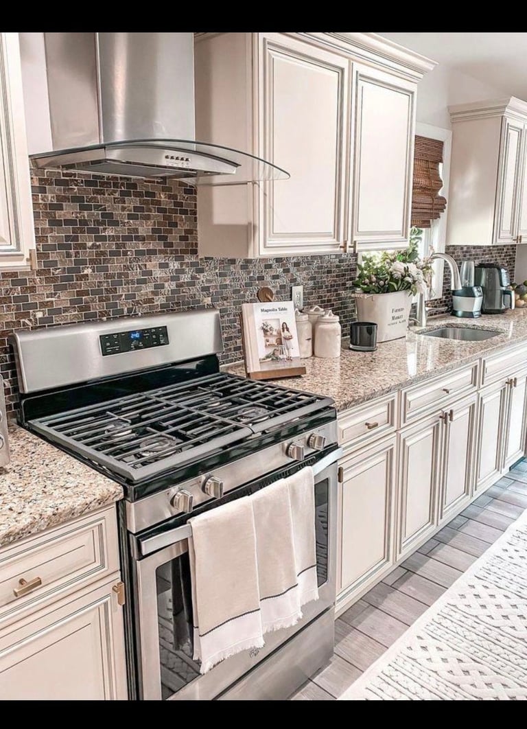 Modern kitchen with white cabinetry, stainless steel stove, brown tile backsplash, and granite countertops with appliances and decor