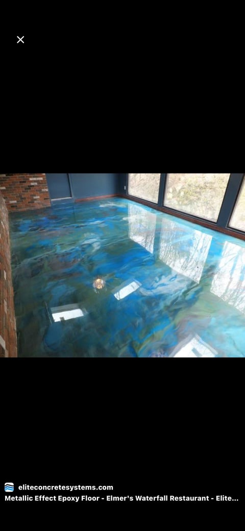 Metallic epoxy floor with blue and turquoise swirled finish in a restaurant interior with brick wall and large windows