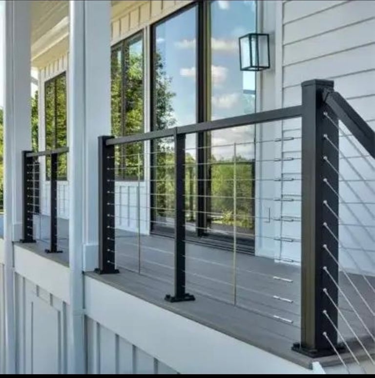 Modern black cable railing on a gray deck with white siding and large windows overlooking green landscape