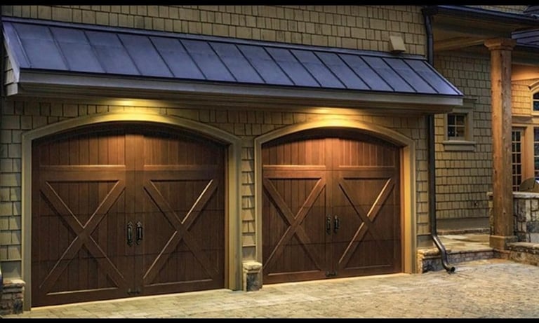 Two-car garage with dark wood X-pattern doors on a brick home at dusk, lit by overhead fixtures
