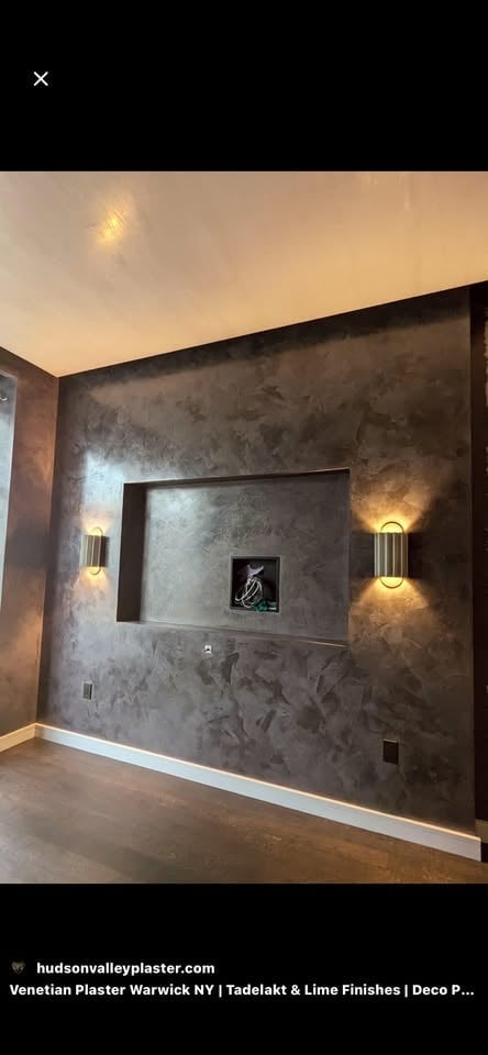 Modern interior wall with dark textured plaster finish, recessed alcove with framed artwork, and decorative wall sconces with warm lighting