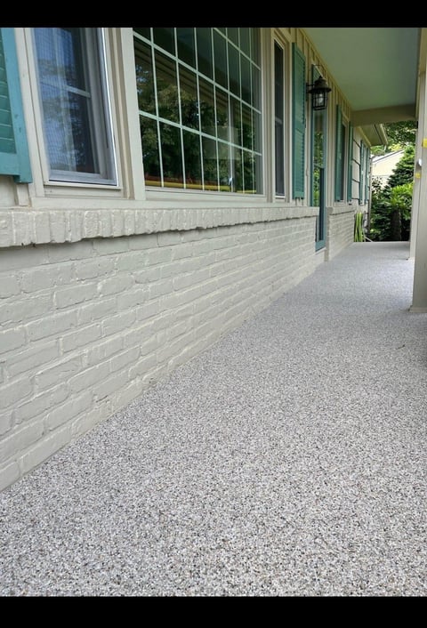 Empty covered porch with white brick walls, large windows, concrete floor, and green roof overhang