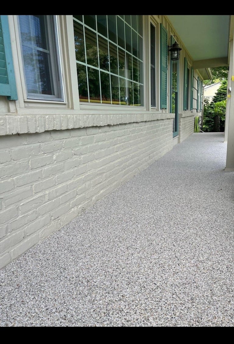 Empty covered porch with white brick walls, large windows, concrete floor, and green roof overhang