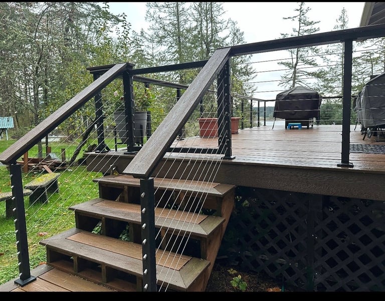 Modern wooden deck with black metal stair railing and cable railings surrounded by trees and landscaping