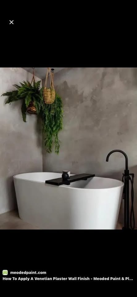 Modern bathroom with white freestanding bathtub, Venetian plaster walls, hanging plants, and black fixtures