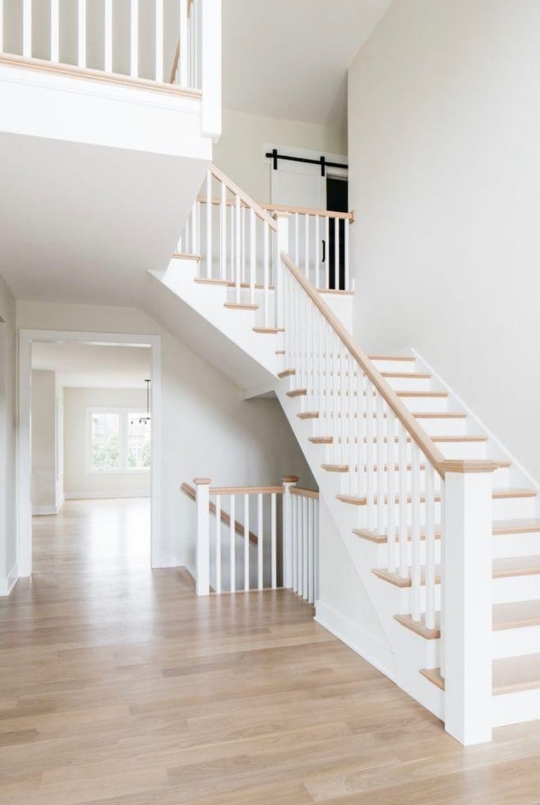 Modern two-story white staircase with wooden steps and light wood railings in a bright, open foyer
