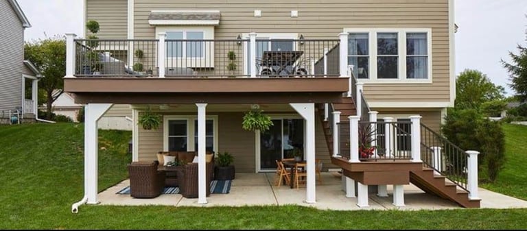 Two-story beige house with white pergola patio, decking, and green lawn in suburban setting