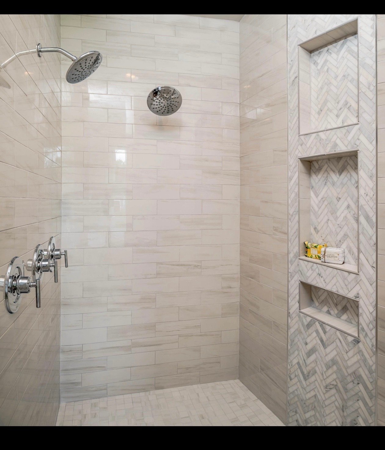 Modern luxury bathroom shower with white subway tile walls, rainfall and handheld showerheads, glass enclosure, and built-in stone shelving