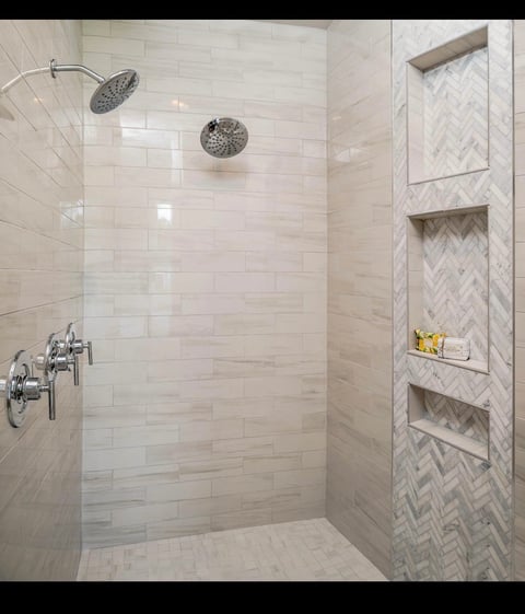 Modern bathroom shower with white subway tile walls, rainfall showerhead, glass enclosure, and built-in stone shelving