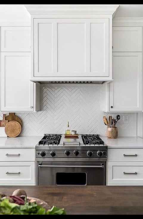 Modern kitchen with white cabinetry, stainless steel gas range, herringbone backsplash