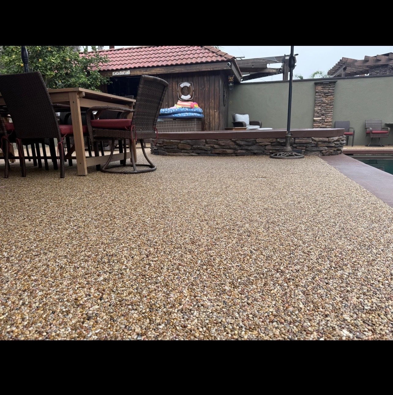 Backyard patio with gravel surface, wooden furniture, shed, and fenced enclosure on sunny day