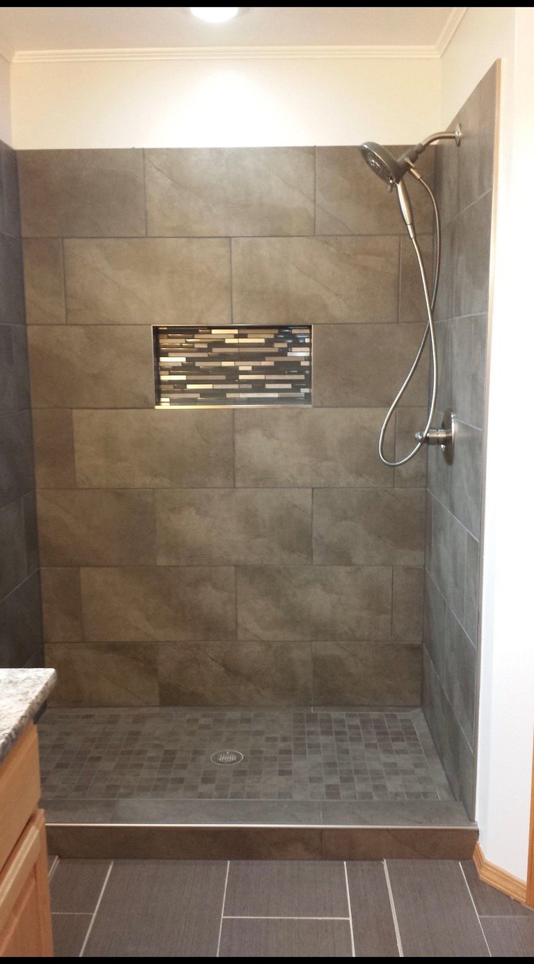 Modern walk-in shower with large gray tile walls, built-in niche, rainfall showerhead, and tiled floor