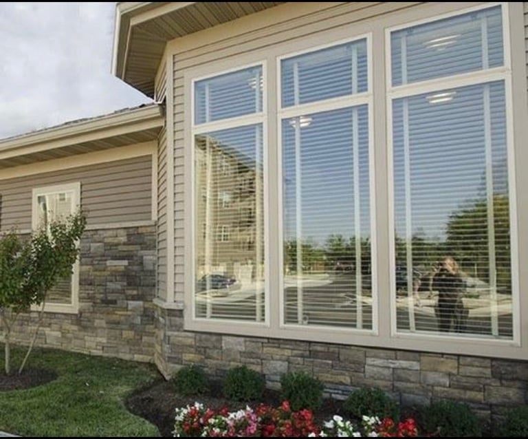 Modern home exterior with large white multi-pane window, stone siding, and red and white flowering plants below