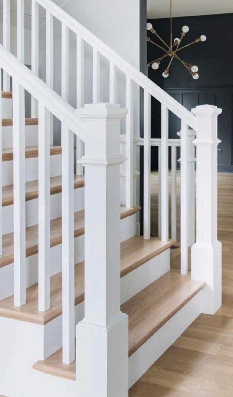 Modern staircase with white balusters and natural wood steps, featuring a dark wall accent and brass pendant light