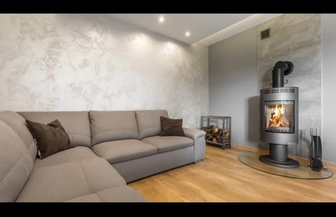 Modern living room with gray sectional sofa, marble accent wall, and cylindrical wood-burning stove
